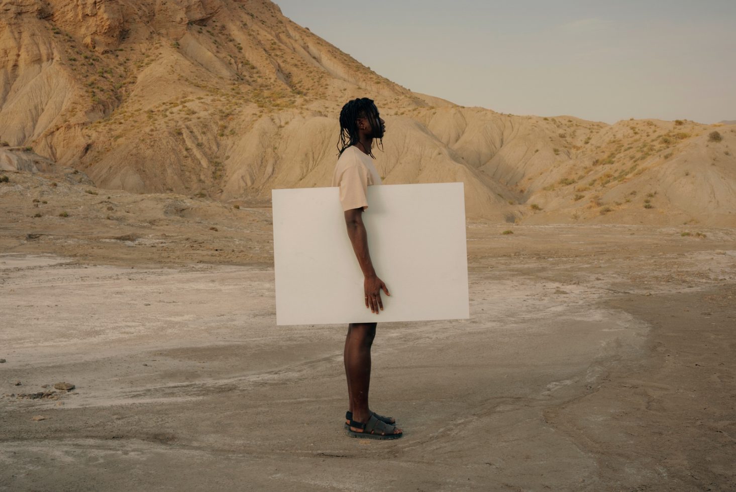 Person holding blank canvas in desert for mockup, side view, space for design, natural light, creative asset.